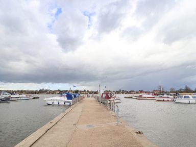A concrete pier with boats moored on either side in a marina with houses in the background at Marsh Bungalow in Lowestoft