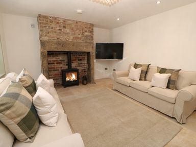 A living room with two beige sofas a stone fireplace with a lit stove and a mounted television at Bramwell House in Corbridge