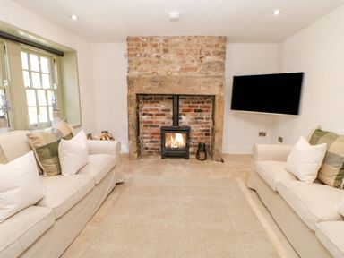 A living room with two sofas facing a brick fireplace with a wood stove and a wall-mounted TV at Bramwell House in Corbridge