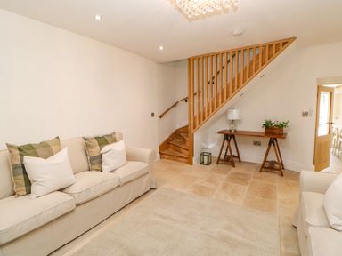 A sitting room with two sofas and a stair railing with a wooden table and lamp at Bramwell House in Corbridge