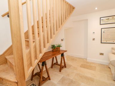 A wooden staircase with a wooden table underneath holding a plant next to a tiled floor at Bramwell House in Corbridge