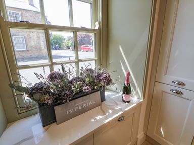 A window sill with a flower arrangement a bottle of pink champagne and two glasses at Bramwell House in Corbridge