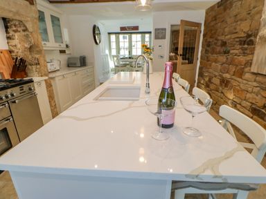 A kitchen with a marble island countertop with a bottle and two glasses a stone wall and white cabinets at Bramwell House in Corbridge