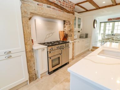 A kitchen with a stove oven set in a stone and brick alcove with white cabinets and a countertop at Bramwell House in Corbridge