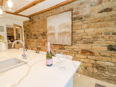 A kitchen island with a bottle of champagne and two glasses against a stone wall with a painting at Bramwell House in Corbridge