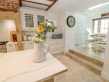 A kitchen with a white counter with a flower vase and a dining area with white chairs at Bramwell House in Corbridge