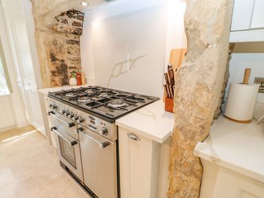 A kitchen with a stainless steel gas stove and oven surrounded by stone and white countertops at Bramwell House in Corbridge
