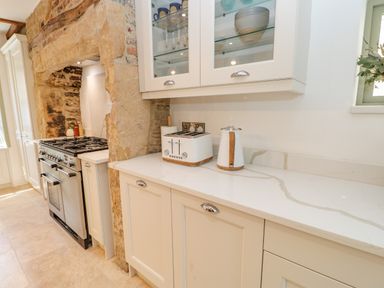 A kitchen with a stone fireplace housing a stove and a countertop with a toaster and a kettle at Bramwell House in Corbridge