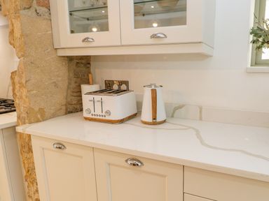 A kitchen counter with a toaster, a kettle, and a paper towel holder with cabinets and a stone wall at Bramwell House in Corbridge