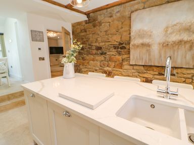 A kitchen island with a white countertop a sink a faucet and a vase with flowers against a stone wall at Bramwell House in Corbridge