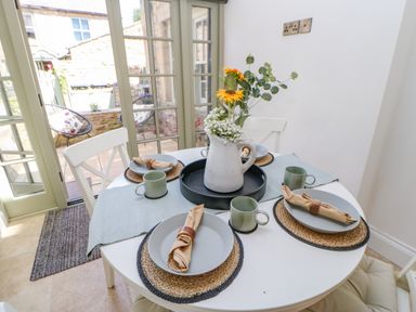 A dining table set with plates mugs and napkins and a flower vase near glass doors at Bramwell House in Corbridge