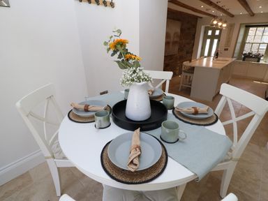 A dining table set with plates mugs and napkins with a floral centerpiece in a kitchen at Bramwell House in Corbridge