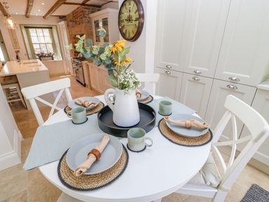 A kitchen with a round dining table set with plates mugs and napkins with a vase of flowers at Bramwell House in Corbridge