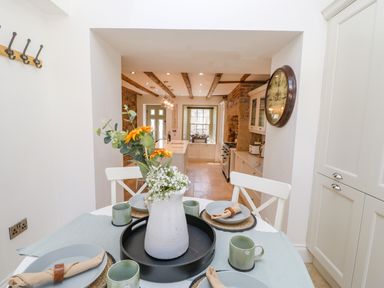 A kitchen dining area with a round table set with plates mugs and napkins and a vase of flowers on the table at Bramwell House in Corbridge