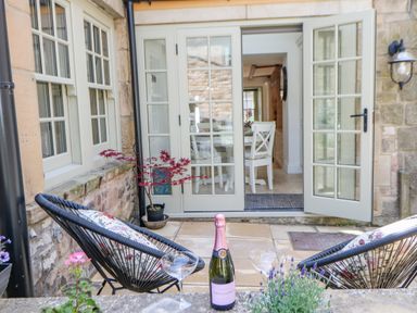 A small patio with two black chairs a bottle of champagne two glasses and an open door leading to a dining area at Bramwell House in Corbridge