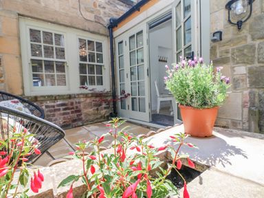 A stone patio with potted plants and outdoor chairs next to glass doors leading inside at Bramwell House in Corbridge