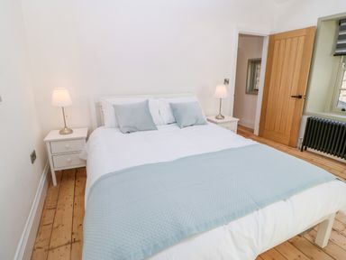 A bedroom with a white bed and light blue bedding between two white bedside tables with lamps at Bramwell House in Corbridge