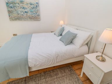 A bedroom with a bed white and blue bedding pillows a white nightstand with a lamp and a painting on the wall at Bramwell House in Corbridge