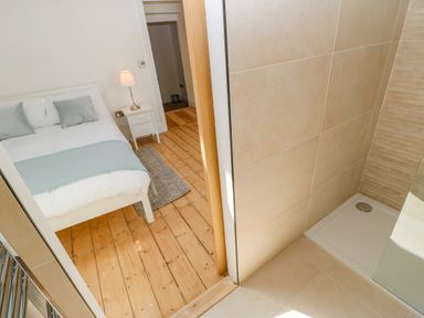 A bedroom with a bed next to a small nightstand and table lamp next to a bathroom with a tiled shower tray at Bramwell House in Corbridge