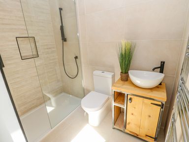 A bathroom with a glass shower enclosure a toilet a wooden vanity with a round sink and plant at Bramwell House in Corbridge