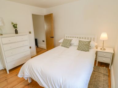 A bedroom with a double bed white dresser and bedside table with lamp at Bramwell House in Corbridge