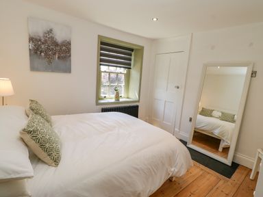 A bedroom with a bed pillows lamp window door and full length mirror at Bramwell House in Corbridge