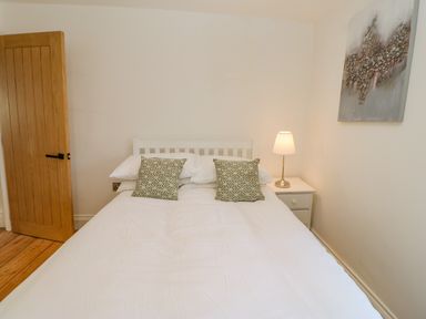 A bedroom with a double bed two patterned pillows a nightstand with a lamp a wooden door and a wall painting at Bramwell House in Corbridge