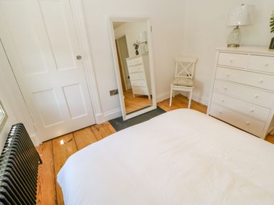 A bedroom with a white bedspread a white dresser with a lamp a white chair and a full length mirror at Bramwell House in Corbridge