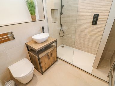 A bathroom with a toilet wooden vanity with a vessel sink and a glass shower enclosure at Bramwell House in Corbridge