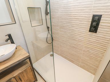 A shower area with glass enclosure a handheld showerhead and control panel next to a wooden vanity with a white vessel sink and black faucet in a bathroom at Bramwell House Corbridge