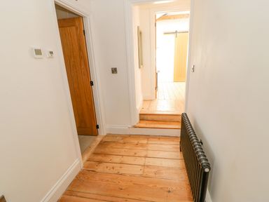 A hallway with wooden floors a black radiator and a wooden door at Bramwell House in Corbridge