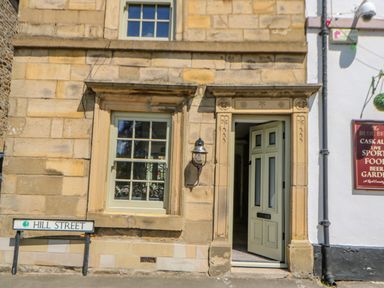 A stone building facade with a window and an open door next to a Hill Street sign