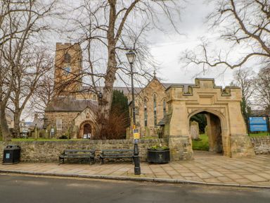 A stone church with a clock tower surrounded by leafless trees benches and a stone archway at Bramwell House in Corbridge
