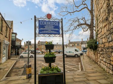 A street scene with a Corbridge town information sign and parked cars at Bramwell House in Corbridge
