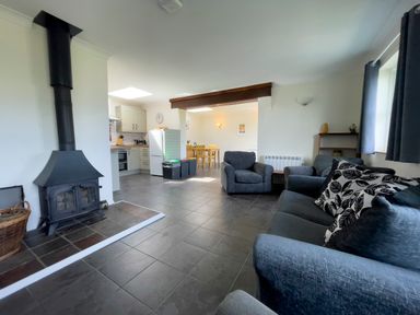 A living room with armchairs a sofa a wood burning stove and a kitchen with a dining table at Ty Coed @ Canllefaes in Penparc near Cardigan