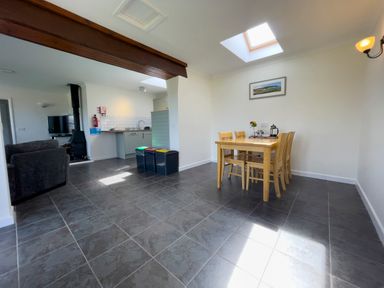 A dining area with a wooden table and chairs next to a kitchen with recycling bins and a living area at Ty Coed @ Canllefaes Penparc near Cardigan