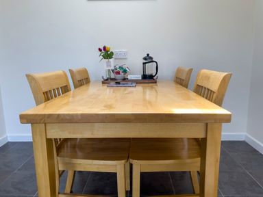 A wooden dining table with four chairs and a tray holding a coffee press, snacks, and flowers at Ty Coed @ Canllefaes in Penparc near Cardigan