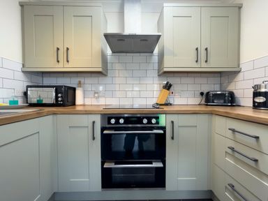 A kitchen with wooden countertops white tiled backsplash cabinets oven microwave toaster and knife block at Ty Coed @ Canllefaes Penparc near Cardigan