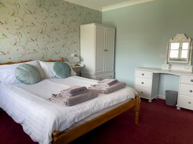 A bedroom with a wooden bed, white wardrobe, white dressing table with mirror, and folded towels on bed at Ty Coed @ Canllefaes in Penparc near Cardigan