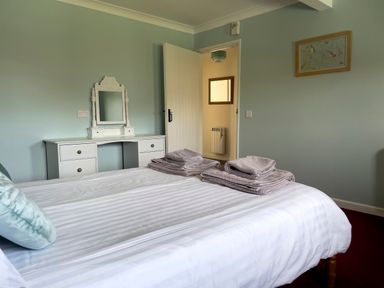 A bedroom with a bed and folded towels on it a vanity table with a mirror an open door and a picture on the wall at Ty Coed @ Canllefaes in Penparc near Cardigan