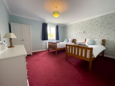 A bedroom with two single wooden beds a white dresser a white wardrobe and a window with dark curtains at Ty Coed @ Canllefaes in Penparc near Cardigan
