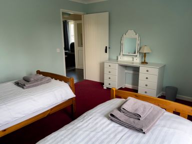 A bedroom with two single wooden beds with folded towels on them next to a white dresser with a mirror and a table lamp at Ty Coed @ Canllefaes Penparc near Cardigan