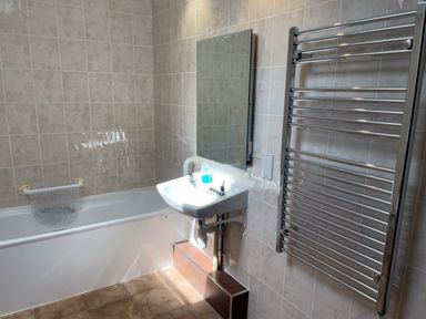 A bathroom with a bathtub a wall-mounted sink a mirror and a towel radiator at Ty Coed @ Canllefaes in Penparc near Cardigan