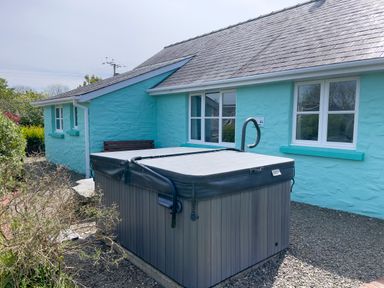 An outdoor hot tub next to a blue house with white windows and a bench at Ty Coed @ Canllefaes in Penparc near Cardigan