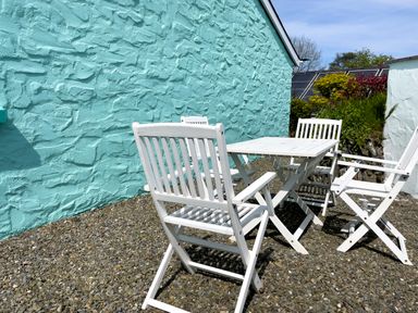 A white outdoor table with four white chairs on a gravel surface next to a turquoise textured wall at Ty Coed @ Canllefaes in Penparc near Cardigan