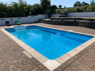 An outdoor swimming pool with stone patio chairs and potted plants at Ty Coed @ Canllefaes in Penparc near Cardigan