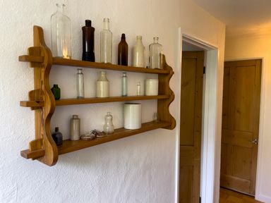 A wooden wall shelf with glass and ceramic bottles in a hallway with wooden doors at The Granary @ Canllefaes in Penparc near Cardigan
