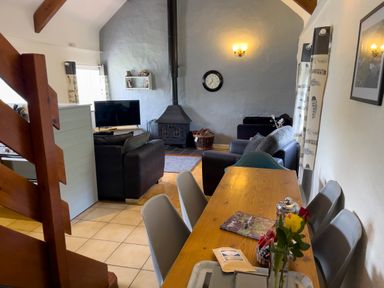 A dining table with chairs next to a living area with sofas a fireplace and a television at The Granary @ Canllefaes in Penparc near Cardigan