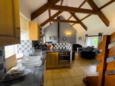 A kitchen with wooden cabinets and a dish drying rack next to a living area with sofas and a clock on the wall at The Granary @ Canllefaes in Penparc near Cardigan