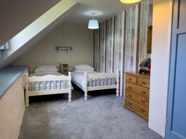 A bedroom with two single beds a wooden chest of drawers and a striped accent wall at The Granary @ Canllefaes Penparc near Cardigan